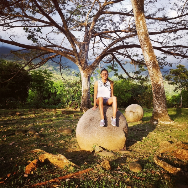 Founder of Simply Happy Wear sitting on a stone sphere surrounded by trees and nature in Costa Rica