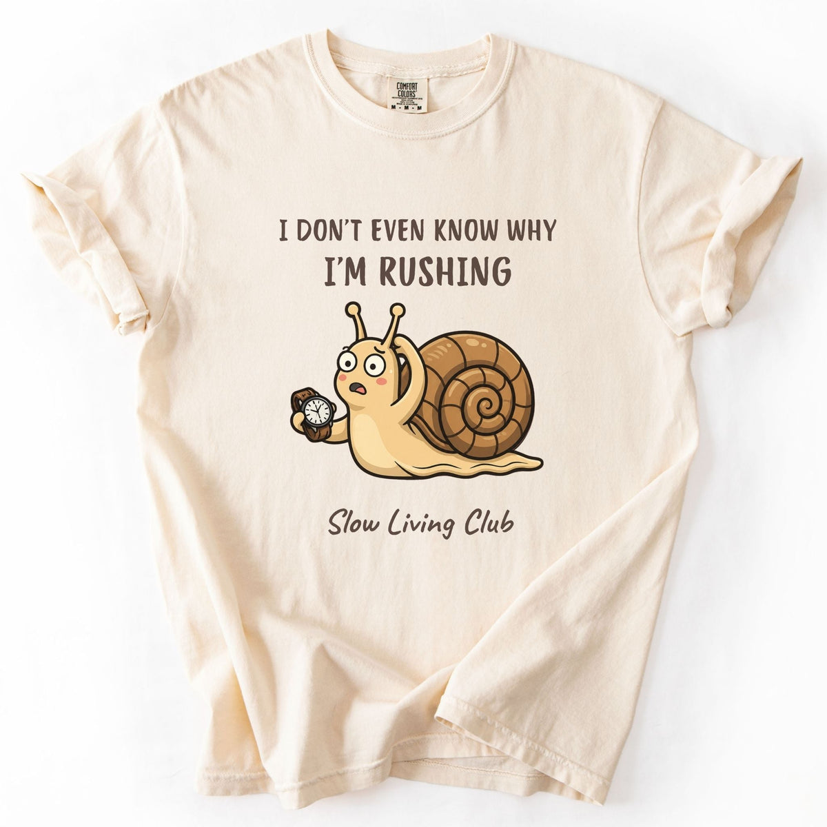 Ivory-colored t-shirt featuring a snail holding a pocket watch with the phrase 'I don't even know why I'm rushing' — Slow Living Club collection by Simply Happy Wear"
