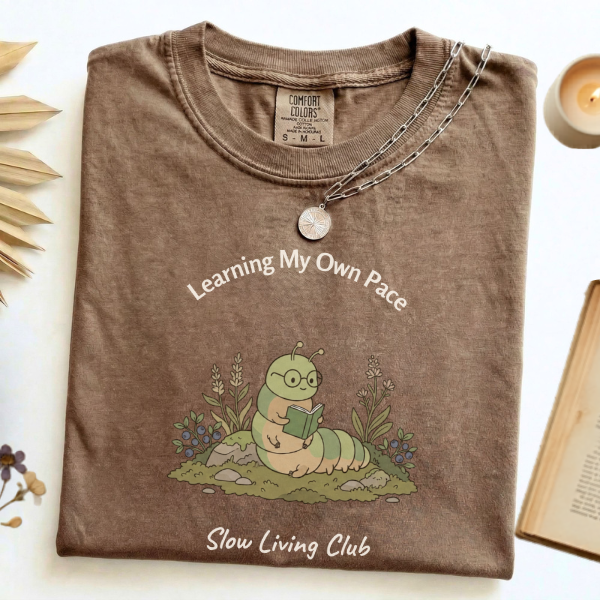 Learning My Own Pace caterpillar reading 
graphic tee in Espresso flat lay with candle 
and book – Slow Living Club Comfort Colors shirt