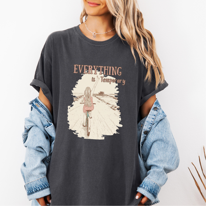 Pepper Comfort Colors graphic tee with a vintage-style illustration of a woman riding a bicycle down an open path and the phrase “Everything is Temporary.”