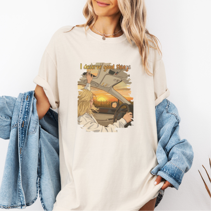 Ivory Comfort Colors graphic tee with a colorful sunset driving illustration and the phrase “I deserve good things.”