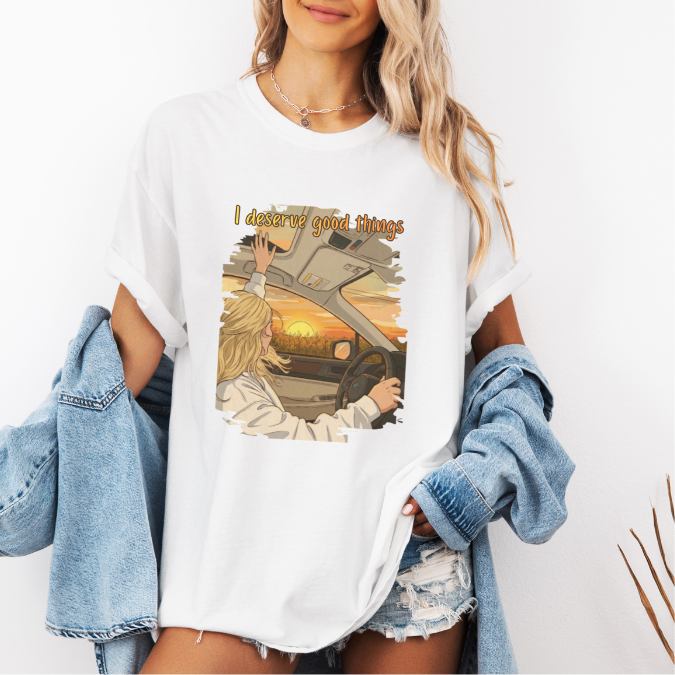 White Comfort Colors graphic tee with a colorful sunset driving illustration and the phrase “I deserve good things.”