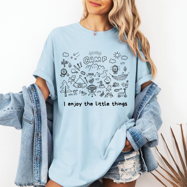 Woman wearing a Chambray Comfort Colors t-shirt with a hand-drawn camp doodle illustration and the text I enjoy the little things, styled with a denim jacket