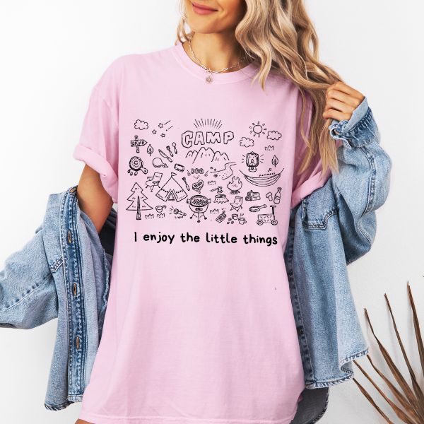 Woman wearing a Blossom Comfort Colors t-shirt with a hand-drawn camp doodle illustration and the text I enjoy the little things, styled with a denim jacket