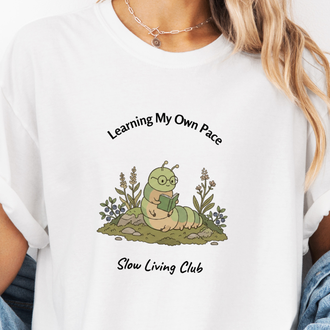 White Slow Living Club t-shirt with Learning My Own Pace caterpillar reading design.