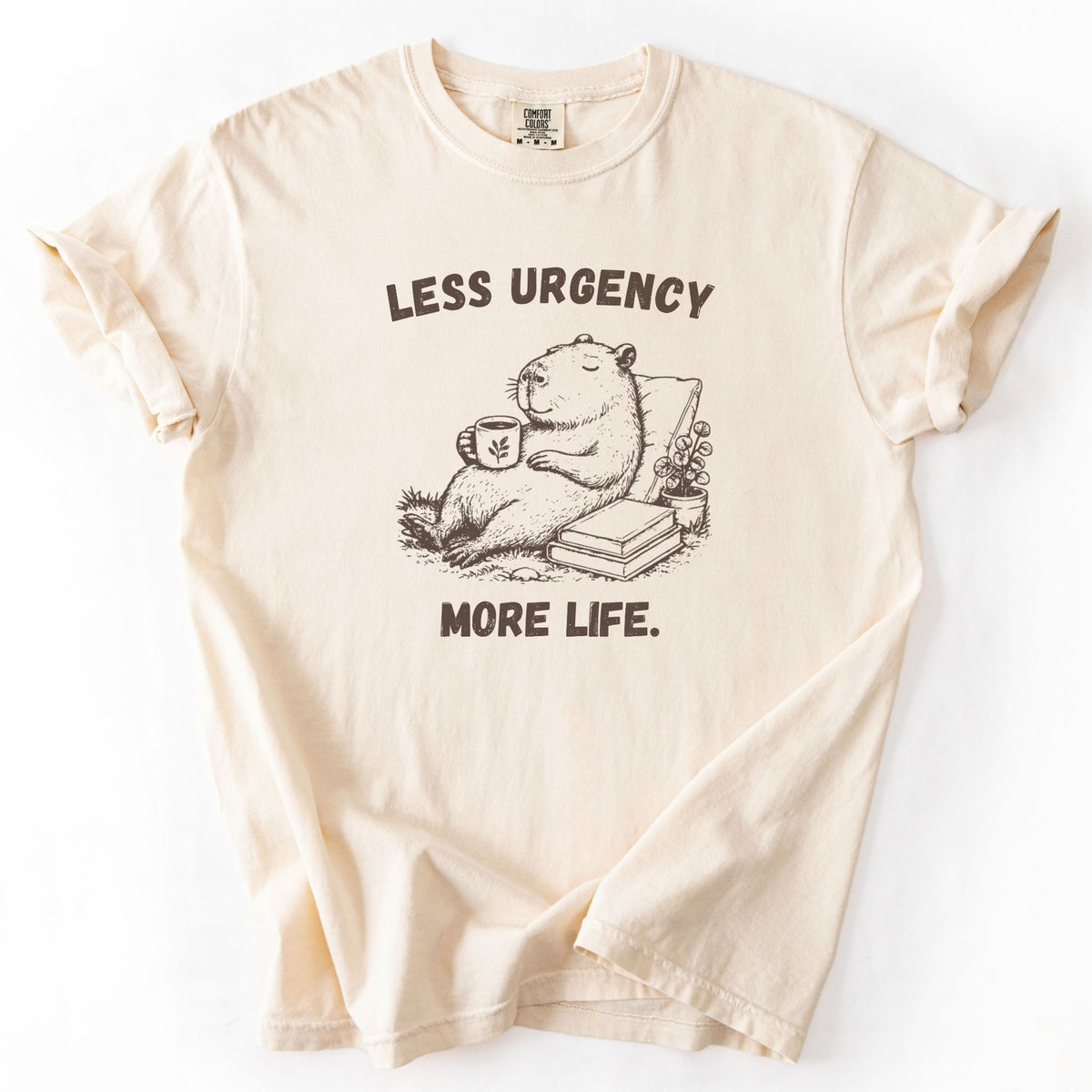 Less Urgency More Life capybara Comfort Colors tee in Ivory, folded flat lay product photo