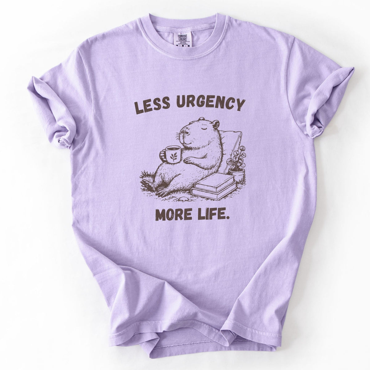 Less Urgency More Life capybara Comfort Colors tee in Orchid lavender, flat lay product photo