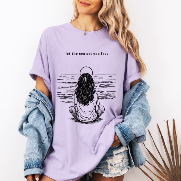 Woman wearing a Orchid Comfort Colors t-shirt with let the sea set you free ocean meditation line art illustration, styled with a denim jacket