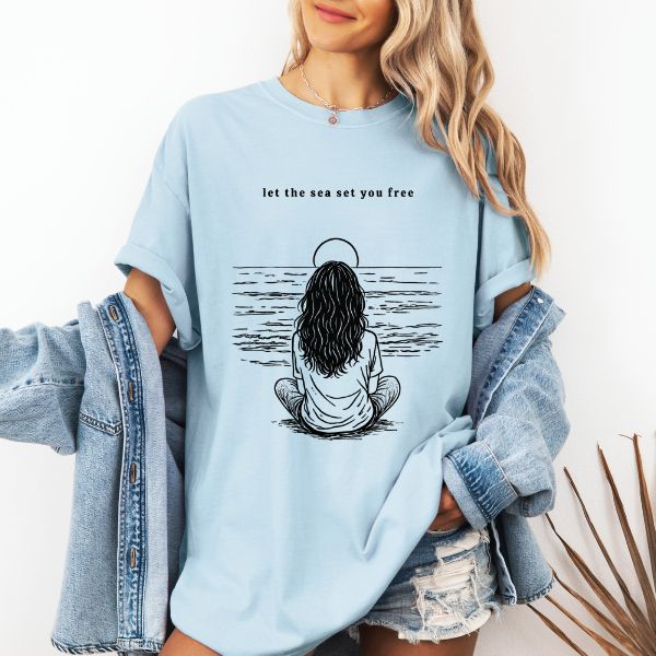 Woman wearing a Chambray Comfort Colors t-shirt with let the sea set you free line art of a woman sitting meditatively facing the ocean, styled with a denim jacket