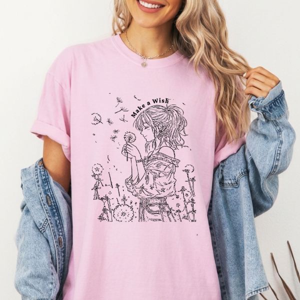 Close-up of a pink Comfort Colors t-shirt featuring a feminine dandelion line art illustration with the text Make a Wish, worn by a woman with a denim jacket