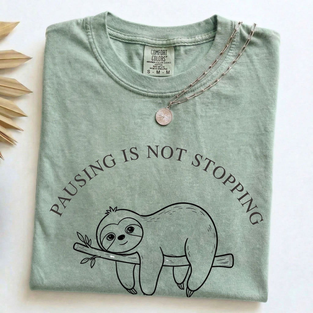 Folded Bay Comfort Colors t-shirt with the Pausing Is Not Stopping minimalist sloth design