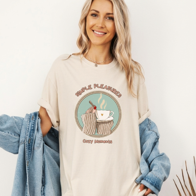 Ivory Comfort Colors graphic tee with a cozy warm drink illustration, sweater sleeves, and the phrase “Simple Pleasures Cozy Moments.”