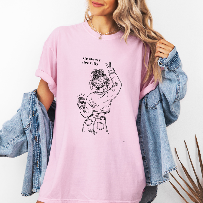 Light pink Comfort Colors graphic tee with a feminine line art illustration of a woman holding coffee and the phrase “sip slowly. live fully.”