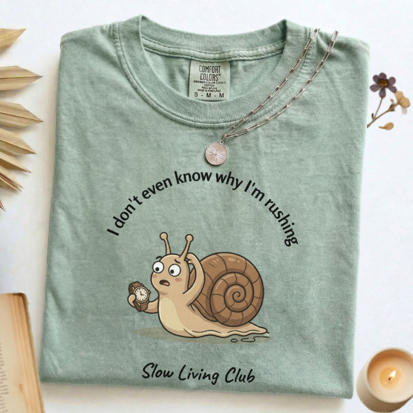 I Don't Even Know Why I'm Rushing snail 
graphic tee in Bay flat lay with candle 
and book – Slow Living Club Comfort Colors shirt
