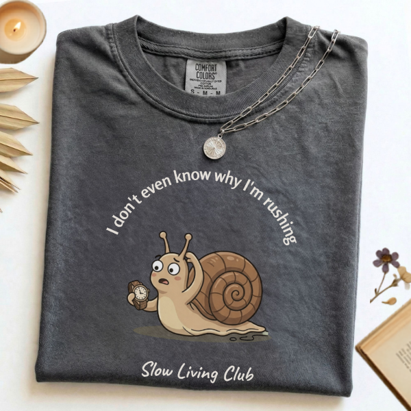 I Don't Even Know Why I'm Rushing snail 
graphic tee in Pepper flat lay with candle 
and book – Slow Living Club Comfort Colors shirt