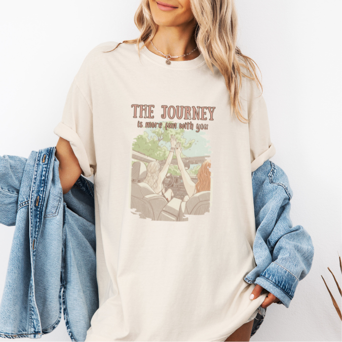Ivory Comfort Colors graphic tee with a vintage-style illustration of two women riding in an open car and the phrase “The journey is more fun with you.”
