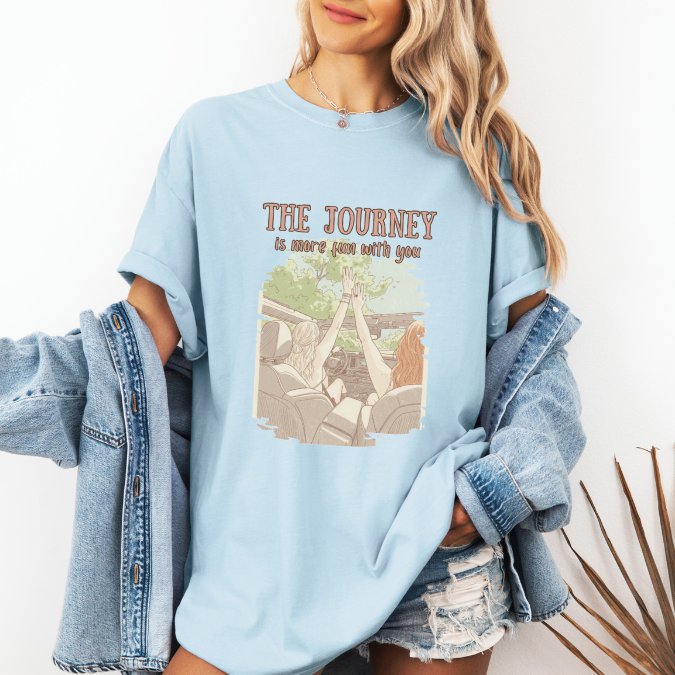 Light Blue Comfort Colors graphic tee with a vintage-style illustration of two women riding in an open car and the phrase “The journey is more fun with you.”