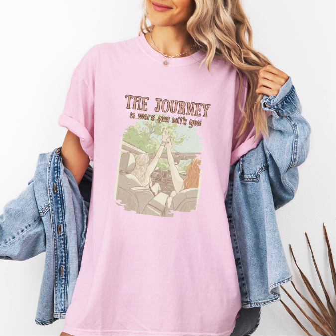 Pink Comfort Colors graphic tee with a vintage-style illustration of two women riding in an open car and the phrase “The journey is more fun with you.”
